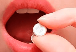 Абортивная таблетка в пальцах перед ртом девушки
